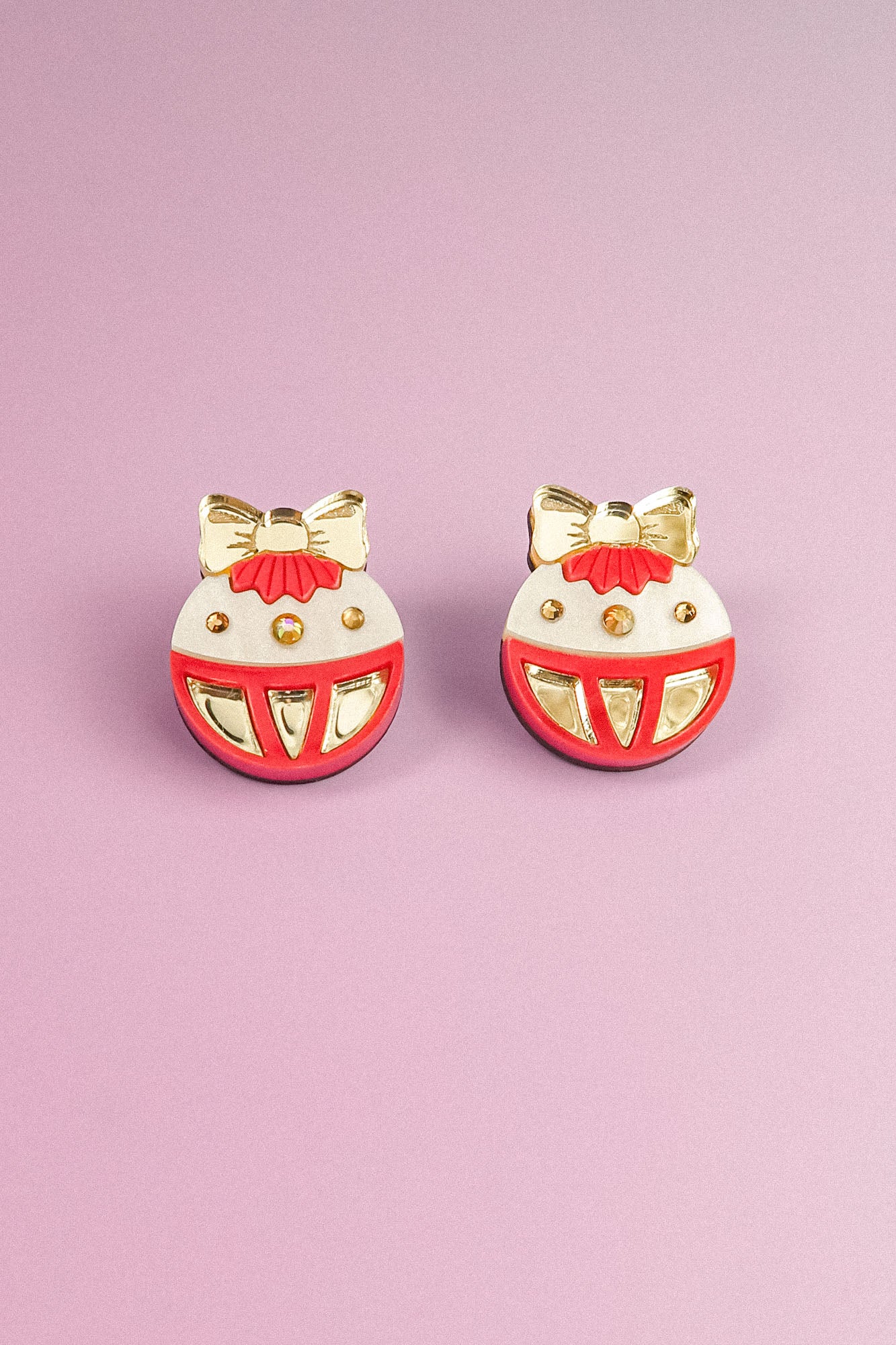 A pair of round, festive earrings with gold bows and accents, red details, and white background, perfect as holiday jewelry. Displayed on a light purple surface, these Poinsettia Statement Hoops add a cheerful touch to any celebration.