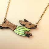 A necklace with a gold chain featuring a Dachshund-shaped pendant, crafted from sustainable wood and wearing a colorful striped sweater.