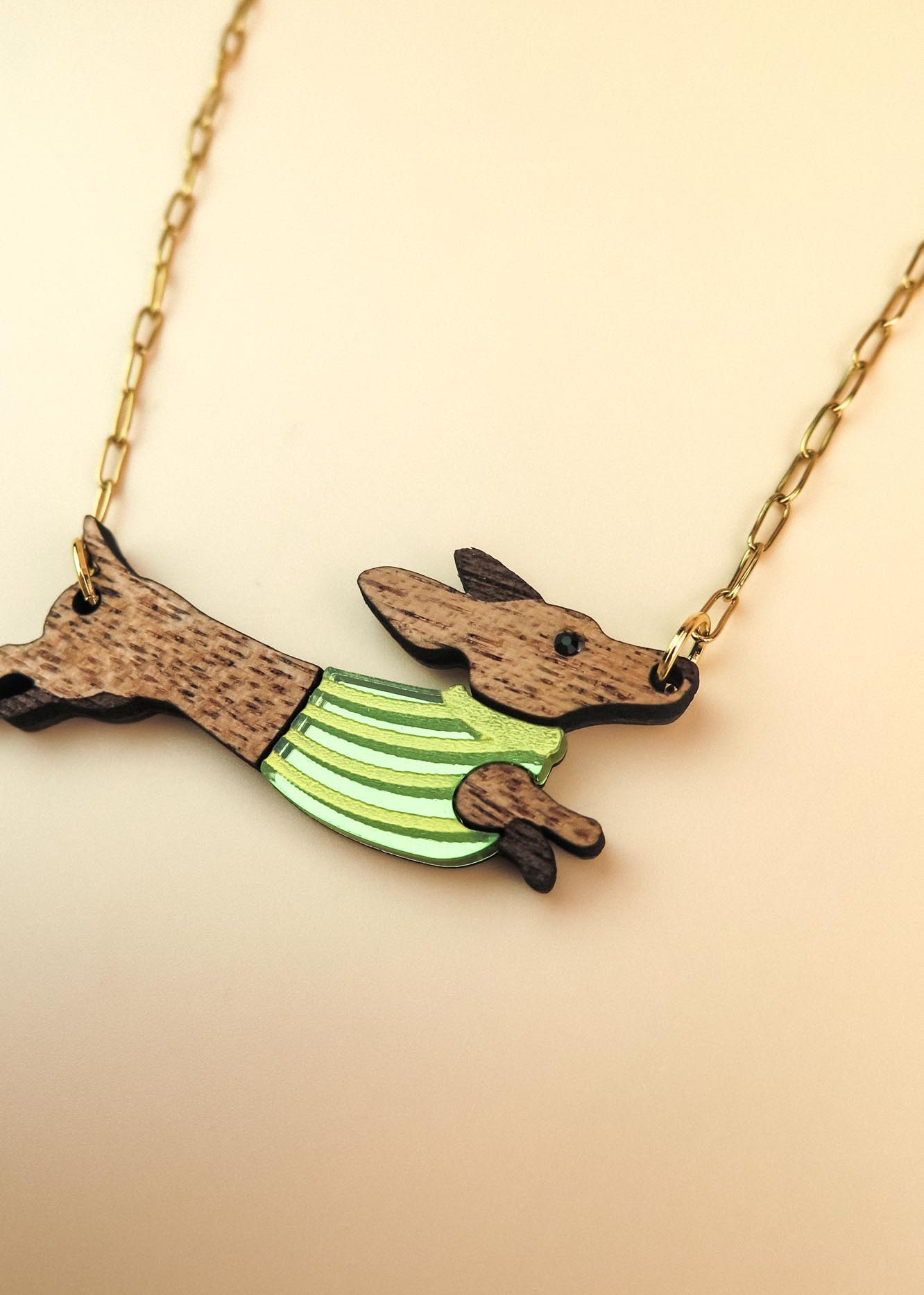 A necklace with a gold chain featuring a Dachshund-shaped pendant, crafted from sustainable wood and wearing a colorful striped sweater.