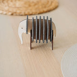A small, elephant-shaped coaster holder made of wood and dark felt stands on a light wooden table, showcasing witty design for furniture protection, surrounded by round woven placemats.