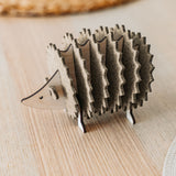A small, wooden hedgehog-shaped coaster holder made of wood and felt sits on a light wooden table with a woven placemat in the background, adding a charming touch to your home decor.
