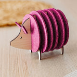A wooden and felt coaster holder shaped like a hedgehog, with pink felt discs forming the body, sits on a light wooden table—a charming housewarming gift for any home.