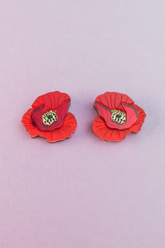 Two lightweight acrylic earrings featuring a vibrant poppy design with black and yellow centers are displayed on a light purple background.