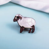 A small, geometric sheep figurine with a white, faceted body and dark brown legs and head, placed on a light blue surface—perfect inspiration for an animal lovers’ Sheep Badge or decorative lapel pin.