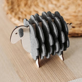 A small wooden sheep figurine with grey felt pieces for wool stands on a light wooden table, adding a charming touch of home decor, with a woven placemat in the background.